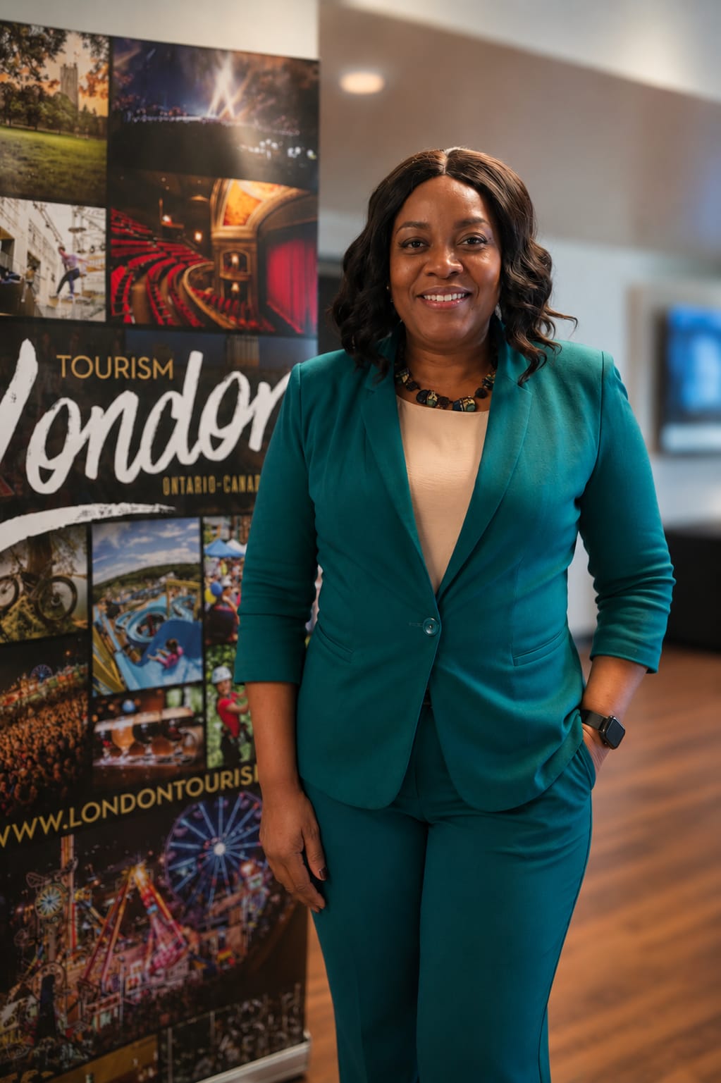 Nadia in a teal suit standing beside a Tourism London banner
