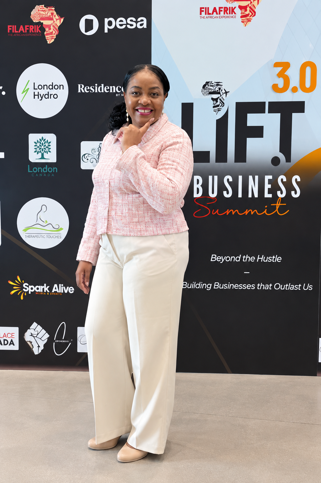 Nadia in a pink jacket standing in front of the LIFT 3.0 Business Summit backdrop