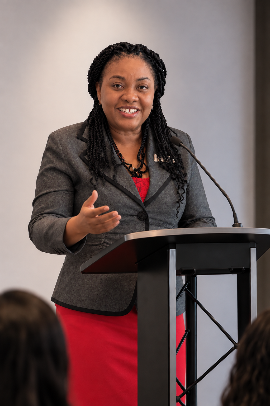 Nadia in a grey jacket and red dress speaking at a podium with a microphone